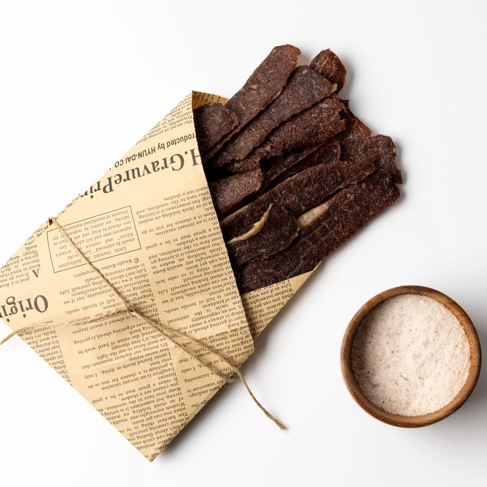 
                  
                    Dried meat sticks on newspaper with a small bowl of seasoning on a white background
                  
                